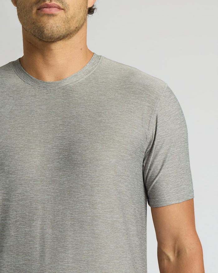 A close-up of a man wearing a light gray heather crew-neck t-shirt against a solid light gray background.