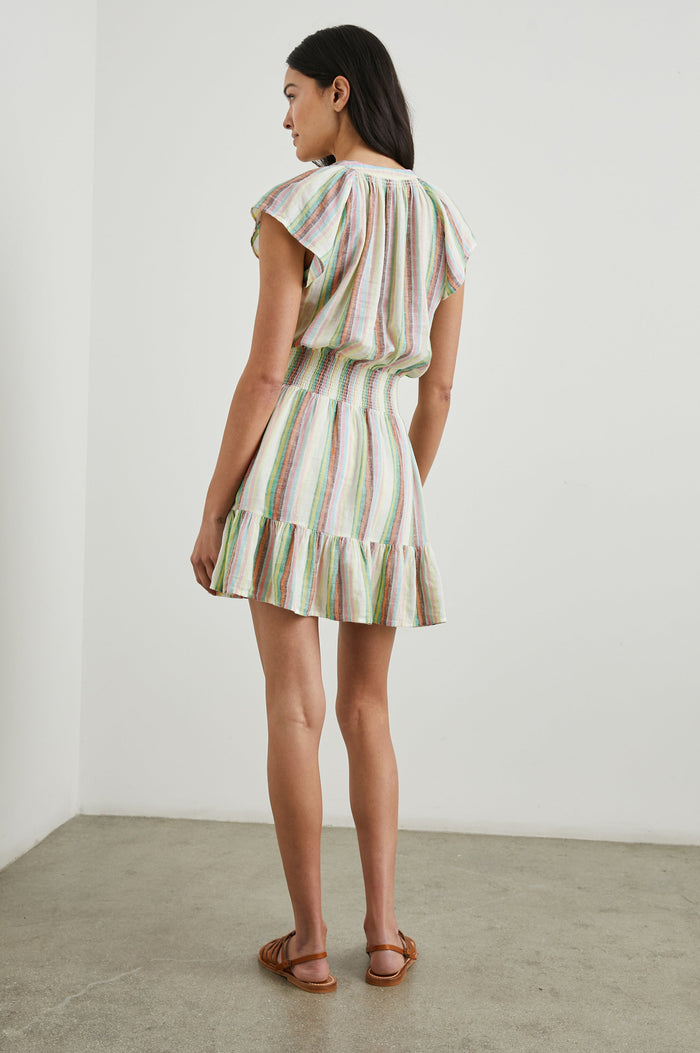 Augustine Short Sleeve Mini Dress with Flutter Cap Sleeves, a V Neck, a Smocked Waist, a Ruffled Hem, and a Placket with Buttons in Palais Stripe Colorway, Vertical Stripes in Green, Yellow, Orange, Brown, Pink, Blue and white - Back Full Body View Featured on Model