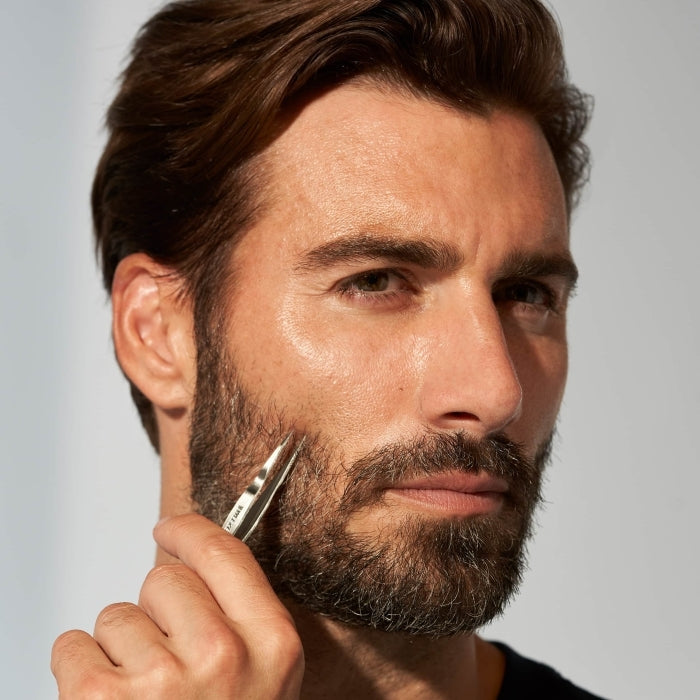 Man using tweezers from the Essential Grooming Kit | Tweezerman to groom facial hair, showcasing precision skincare and body care grooming tools for a well-maintained beard.