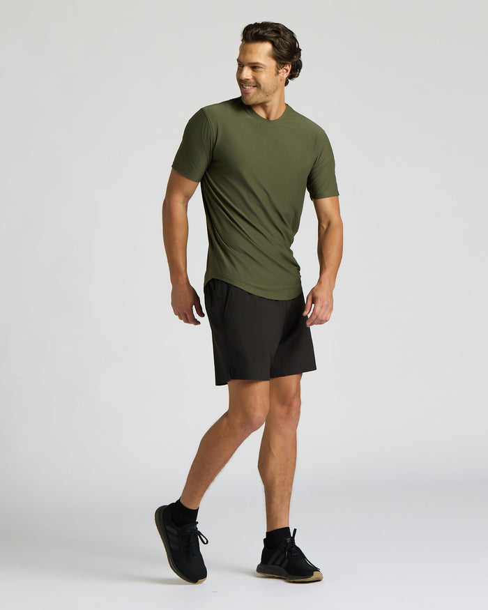 A man modeling an olive green short-sleeve athletic t-shirt and black athletic shorts against a light gray studio background.