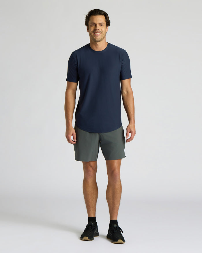 Man wearing a navy t-shirt and gray shorts on a white background