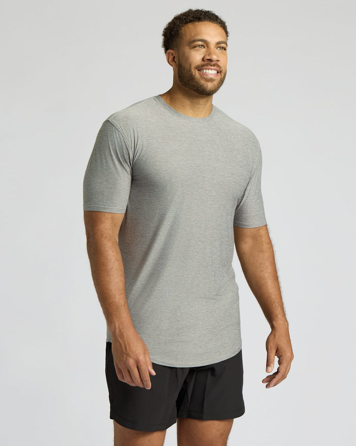 A man wearing a light gray heather crewneck t-shirt and black athletic shorts, standing against a light gray studio background.
