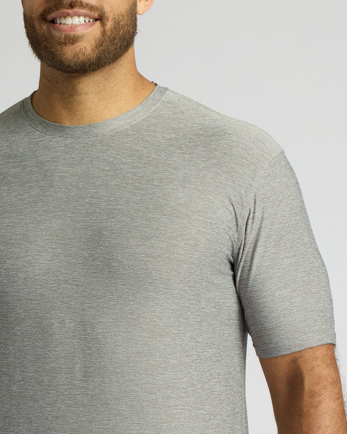 A close-up of a man wearing a light gray heather crew-neck t-shirt against a solid light gray background.