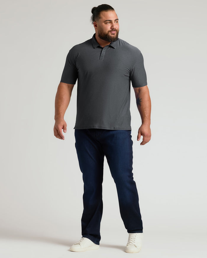 A confident man modeling a charcoal heather gray short-sleeve polo paired with dark jeans and white sneakers, showcasing the Charcoal Heather Gray Active Polo 2.0 in a casual stance.