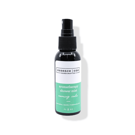 A black spray bottle of Aromatherapy Shower Mist | Essence One with a green and white label, designed for a calming wellness and body care experience.