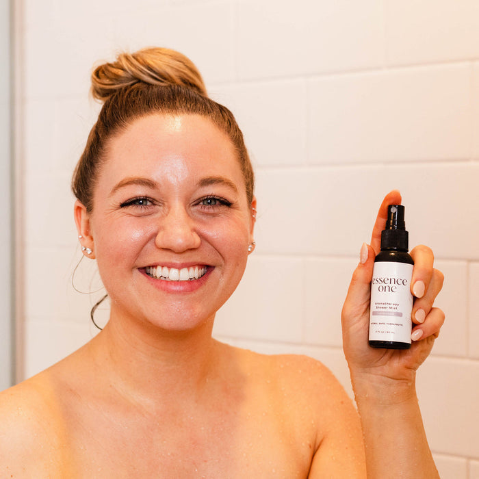 Woman smiling in a shower holding a bottle of Aromatherapy Shower Mist | Essence One, promoting wellness and skincare with a fresh, natural look.