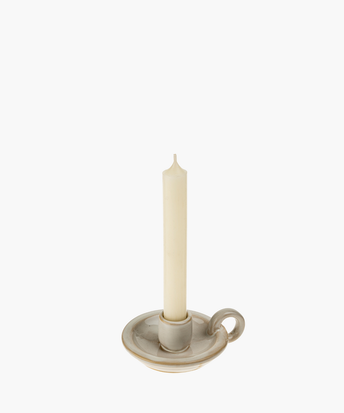 A cream-colored, unlit taper candle stands in a classic ceramic holder with a handle, evoking simplicity and elegance against a plain white background. | SW Home