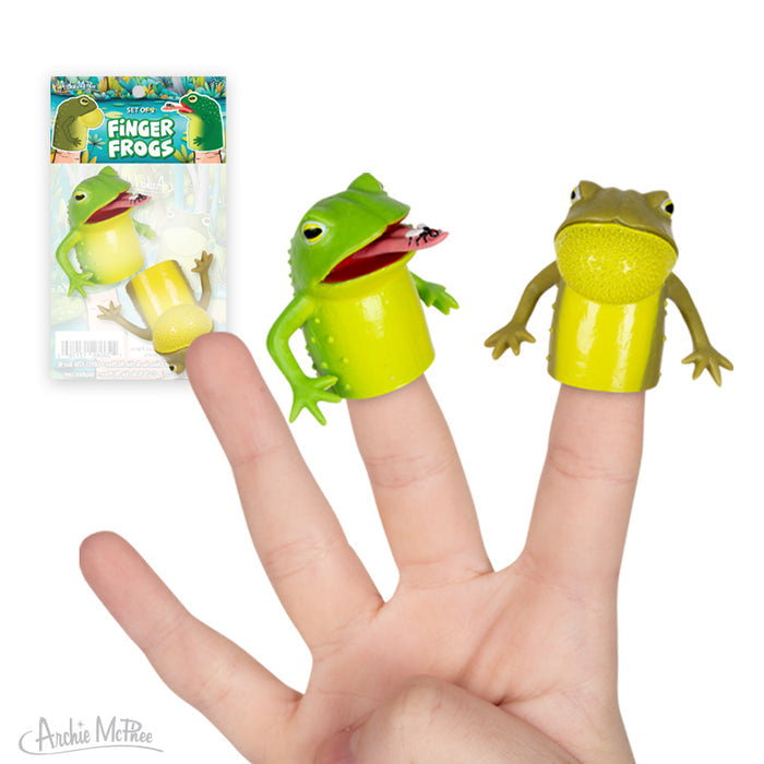 Two green and yellow Finger Frogs finger puppets made of soft vinyl are displayed on fingers, with the Finger Frogs packaging visible in the background.