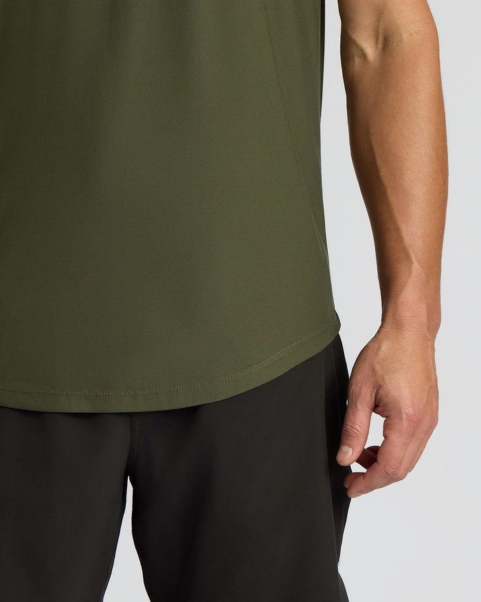Close-up of a person wearing an olive green athletic tank top and black athletic shorts against a light gray studio background.