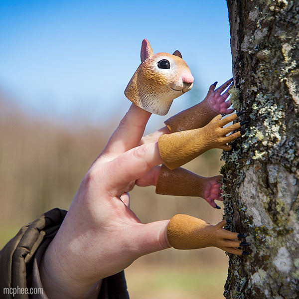 A hand decorated with Handisquirrel finger puppets, positioned as if scaling a tree trunk.