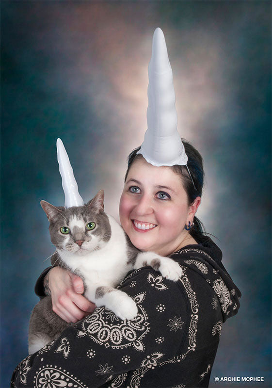 A person and their cat, both wearing Inflatable Unicorn Horns for Cats, pose against a colorful backdrop for a delightful photo.