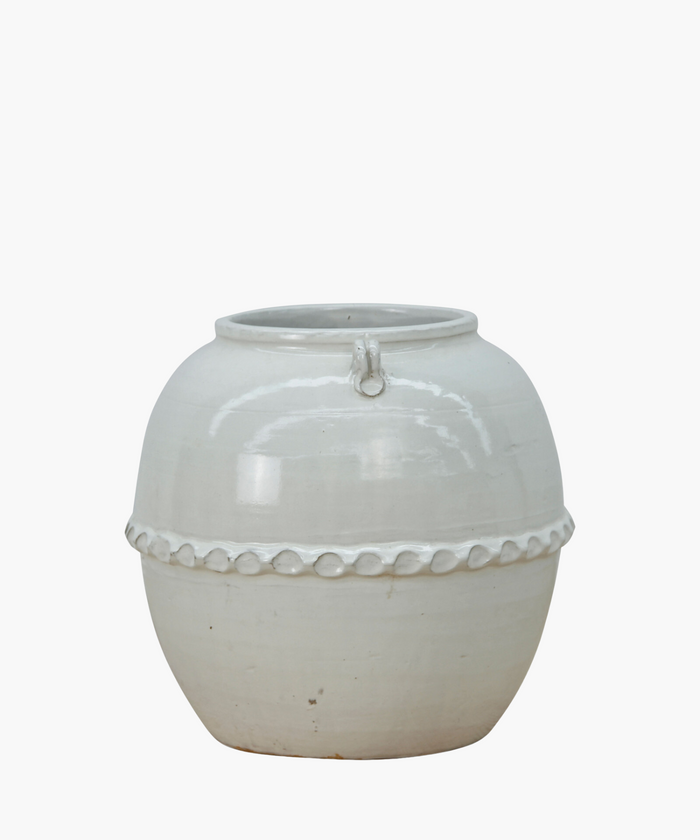 A white ceramic pot with a glossy surface and rounded shape. It features a decorative band with a loop design near the top, giving an elegant look.| Wildwood Home Co.