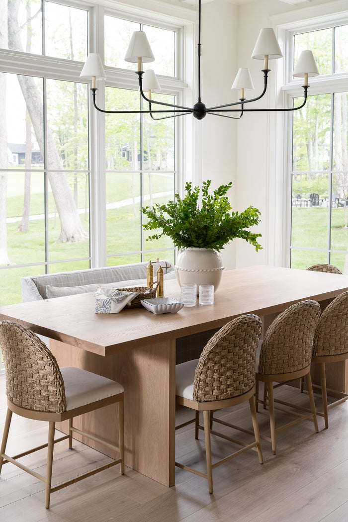 A white ceramic pot with a glossy surface and rounded shape. It features a decorative band with a loop design near the top styled on a kitchen table with greenery. | Wildwood Home Co.