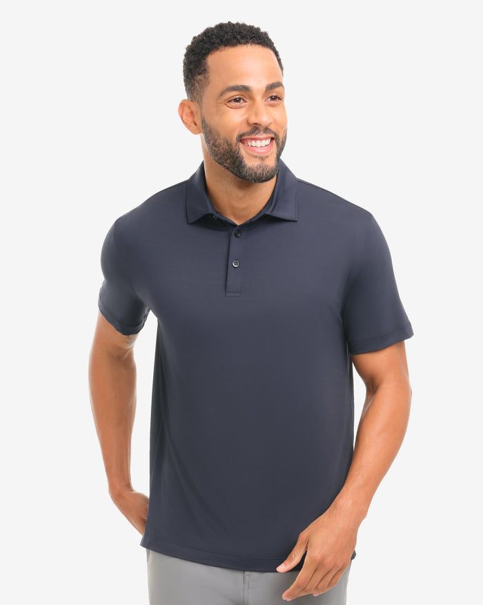 Man wearing a black polo shirt and gray shorts on a white background