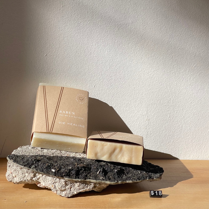 Two bars of Nettle Sabu Soap | Vie Healing displayed on textured black and white stone against a plain wall, highlighting natural skincare and body care products.
