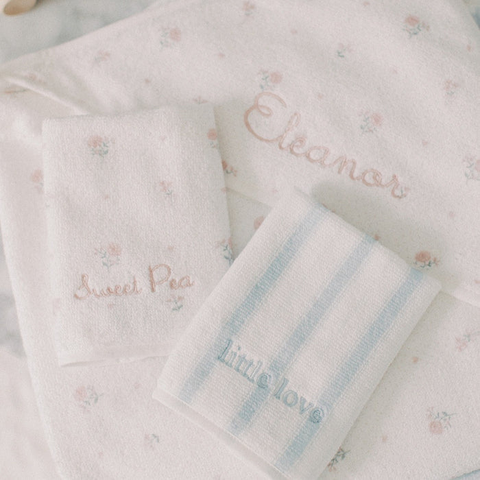 Three personalized baby washcloths in soft pastel colors, including a floral print, a light pink embroidered name, and light blue stripes with a blue embroidered name, arranged on a white background.
