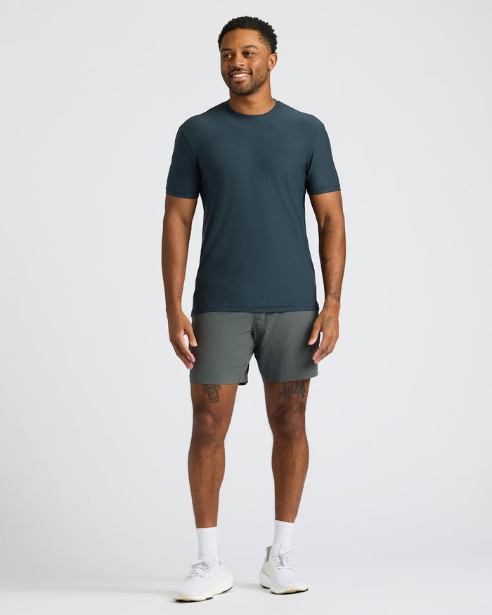 Man wearing a dark green t-shirt and gray shorts on a white background