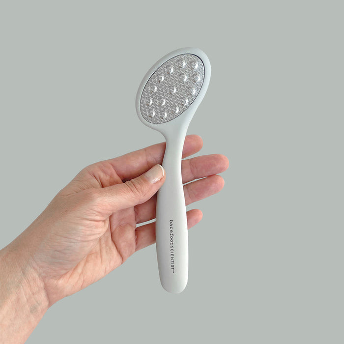 Hand holding the Smooth Things Over | Barefoot Scientist foot care tool with ergonomic handle and textured surface for skincare and body care wellness.