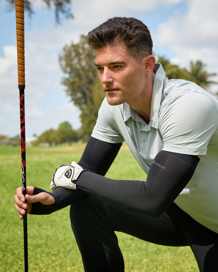 Man on a golf course holding a golf club with trees and sky in the background